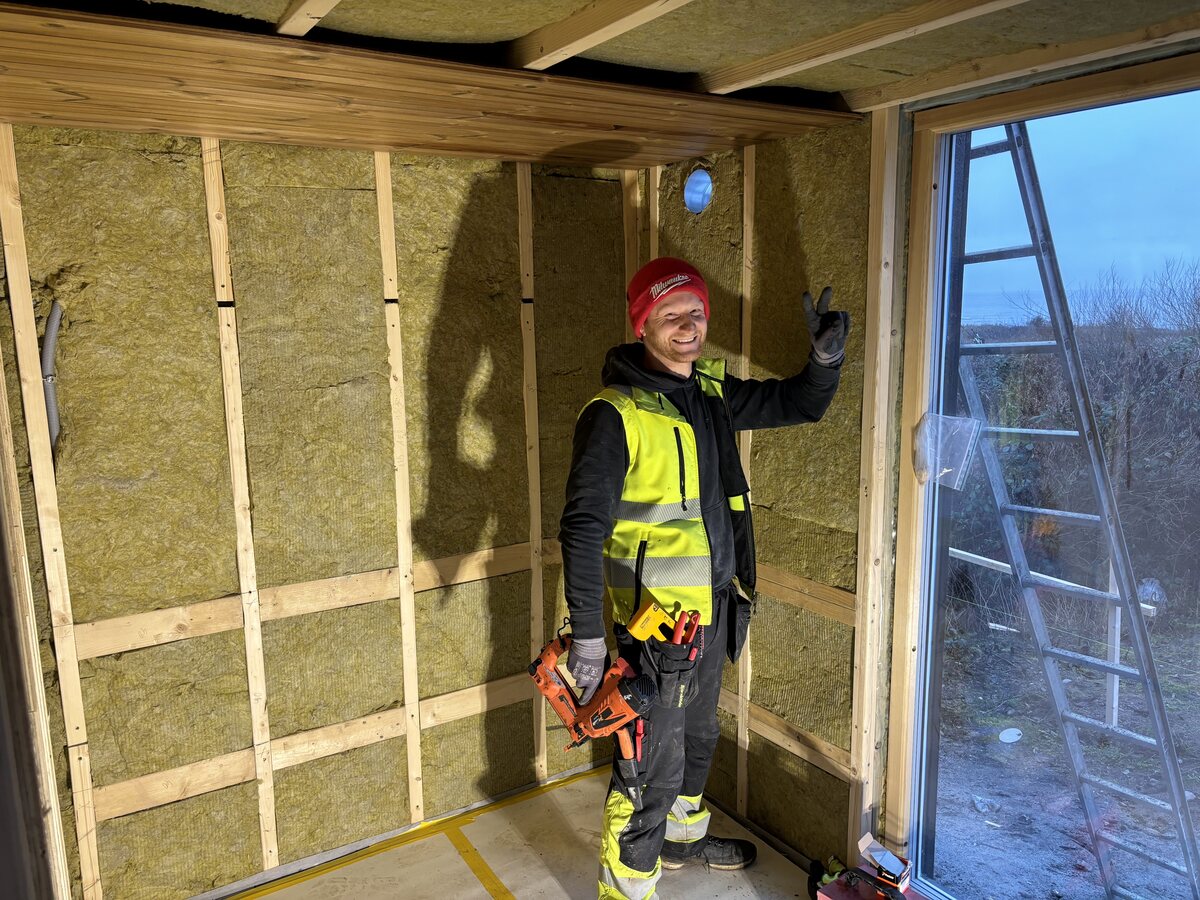 Snickare inne i attefallshuset under bygget, med trästomme och isolering på plats i väggarna.